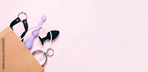 Adult sex toys and accessories purchases on pink background. Anal dildo, butt plug in paper bag. Top view, flat lay.