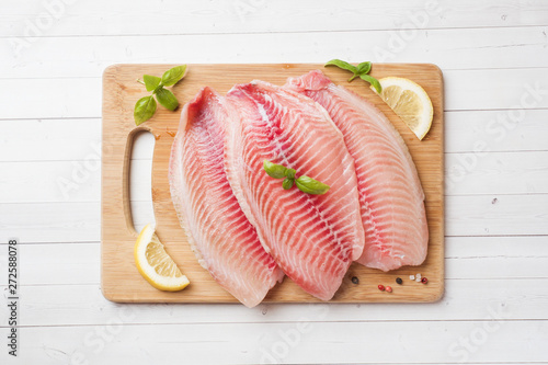 Fotografie Raw fish fillet of tilapia on a cutting Board with lemon and spices