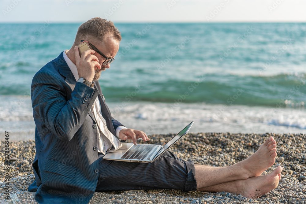 Businessman working with computer and talking on phone on the beach