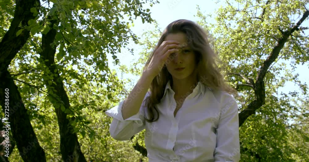 playful young woman is standing in garden in sunny spring day, touching her beautiful hair playful young woman is standing in garden in sunny spring day, touching her beautiful hair