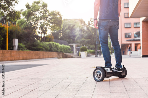 A man in jeans and sneakers on a hoverboard ride in the city. Happy boy riding around at sunset. Modern electronics for relaxation and entertainment. Copy space 