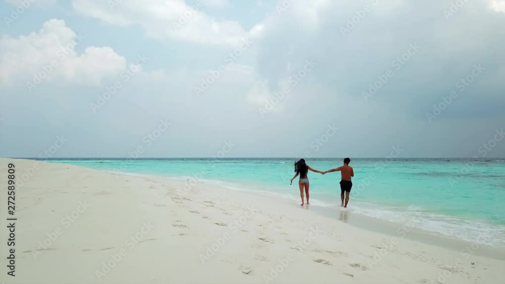 Aerial Approaching White Sand beach to Couple Walking Into Ocean - Vabbinfaru, Maldives Aerial Approaching White Sand beach to Couple Walking Into Ocean - Vabbinfaru, Maldives