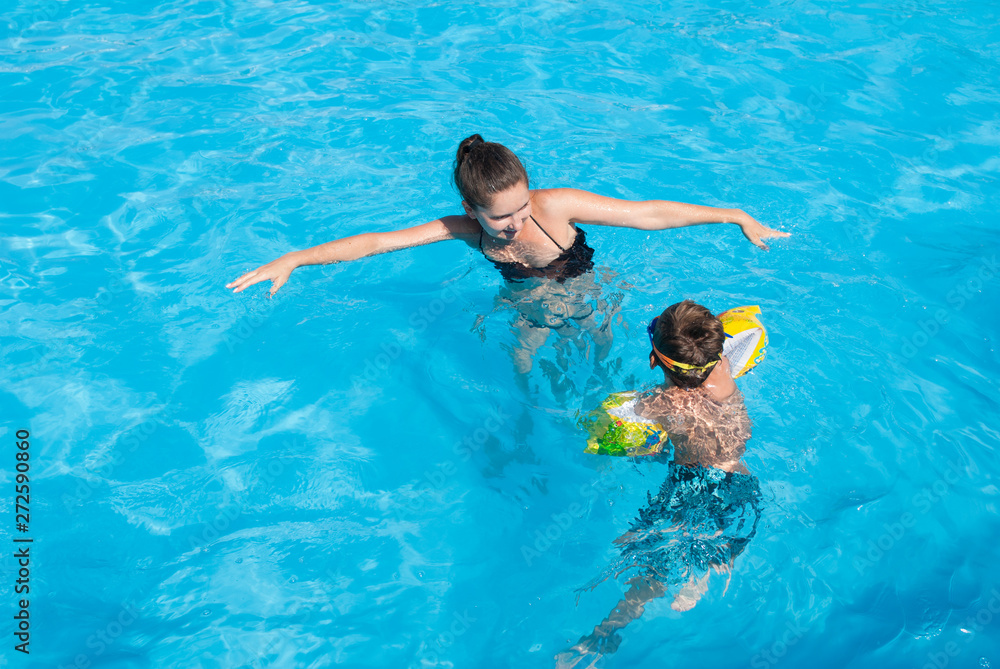 beautiful young adult happy mother woman teaching her little kid to swim in summer azure pool during holiday travel