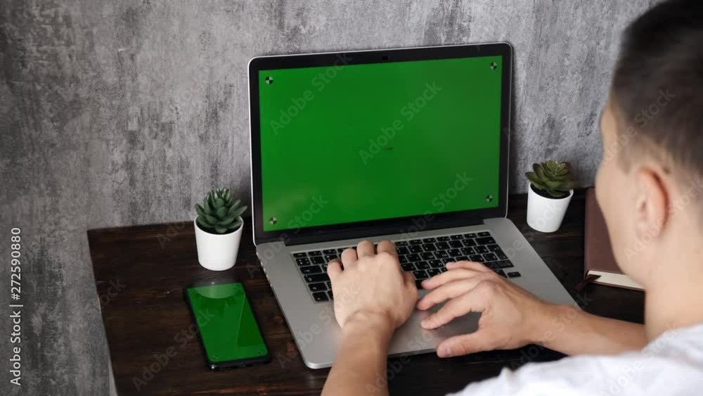 computer closeup with green screen. a man works for a laptop and drinks coffee. Young businessman in office typing text on a laptop with a chroma key to insert. computer closeup with green screen. a man works for a laptop and drinks coffee. Young businessman in office typing text on a laptop with a chroma key to insert.