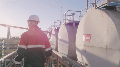 Petrochemical engineer walks along row of cisterns with oil and controls their condition.