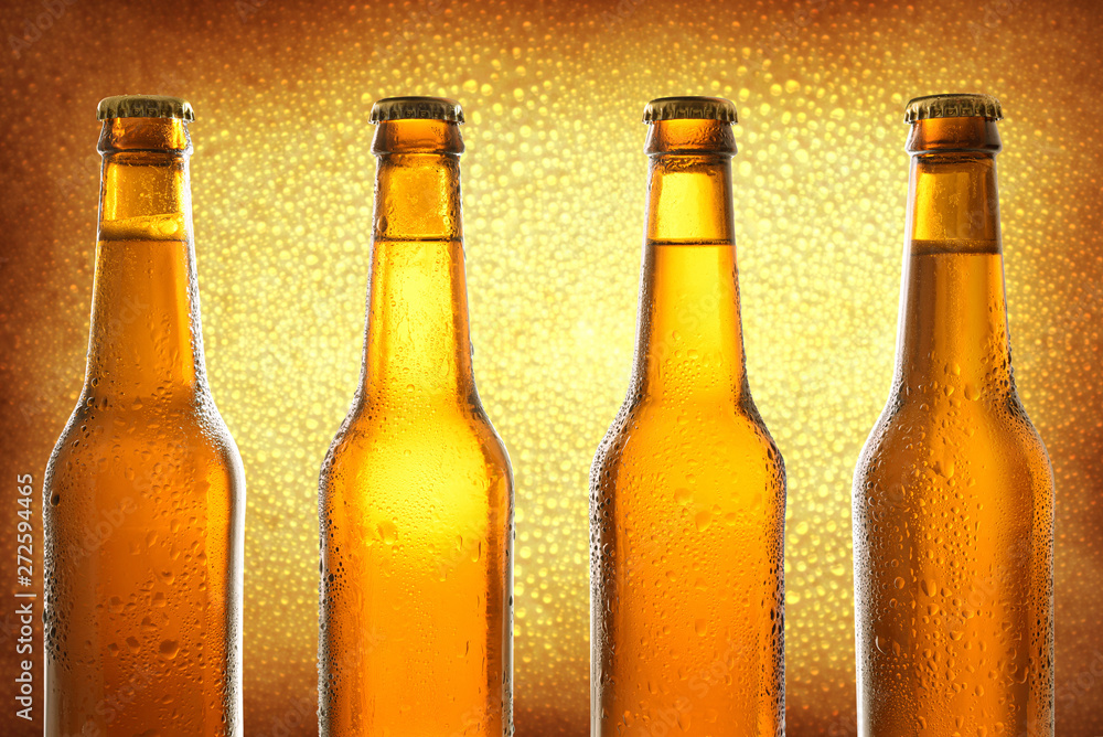 Row of four closed glass bottles with fresh beer on golden background