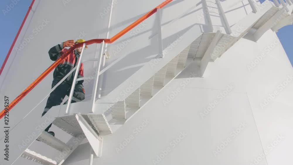 Petrochemical engineer climbs staircase of fuel tank, stops and wipes forehead with his hand Petrochemical engineer climbs staircase of fuel tank, stops and wipes forehead with his hand
