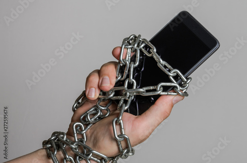 Mobile phone smartphone chained to hands with chains on a light background