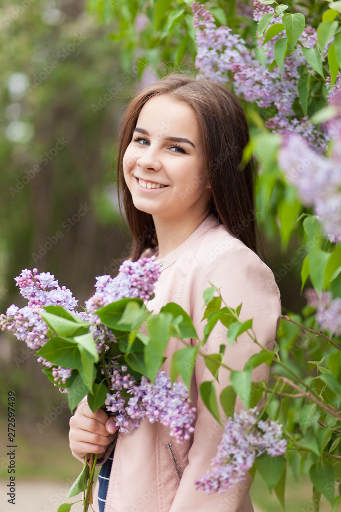 Young beautiful girl stands near the bushes of blooming lilac Young beautiful girl stands near the bushes of blooming lilac