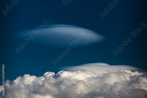 Rare Lenticular cloud Altocumulus lenticularis on top of a cumulus cloud in front of a blue sky photo