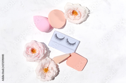 Beautiful pink roses, cosmetic sponge and false eyelashes on the white background.Concept of beauty tools for women