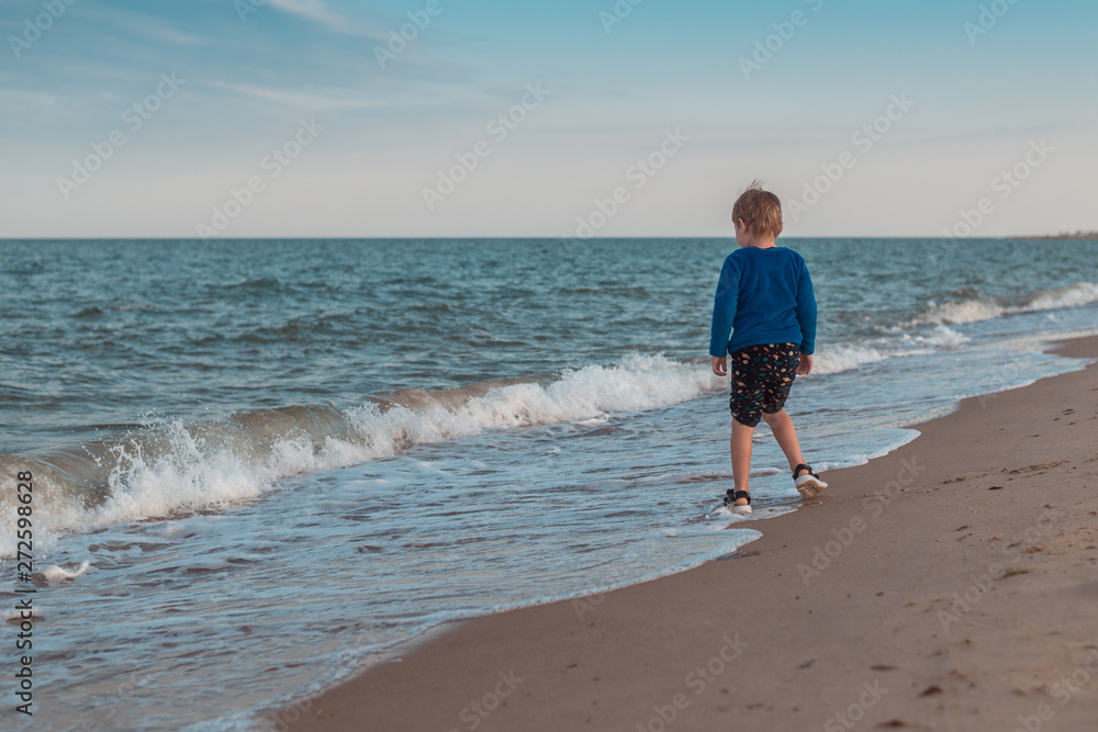 A little boy runs along the coast of the sea, the ocean. Leisure activities in the summer.