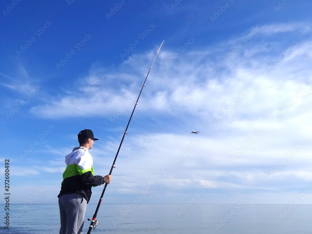 Man with spinning rod fishing in the sea. The plane flying against the sky. seascape. The theme of fishing.