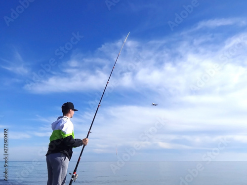 Man with spinning rod fishing in the sea. The plane flying against the sky. seascape. The theme of fishing. © yulliash