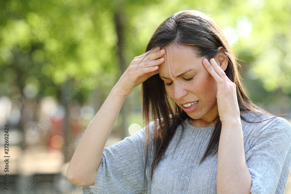 Woman suffering head ache outdoors in a park Woman suffering head ache outdoors in a park