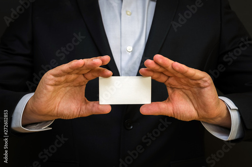 Man wearing a suit holding white business card on black wall bac