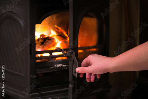 Human hand opening a door of the burning fireplace with wooden l