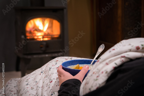 Woman having a hot bowl of vegetable soup at the fireplace. Burn