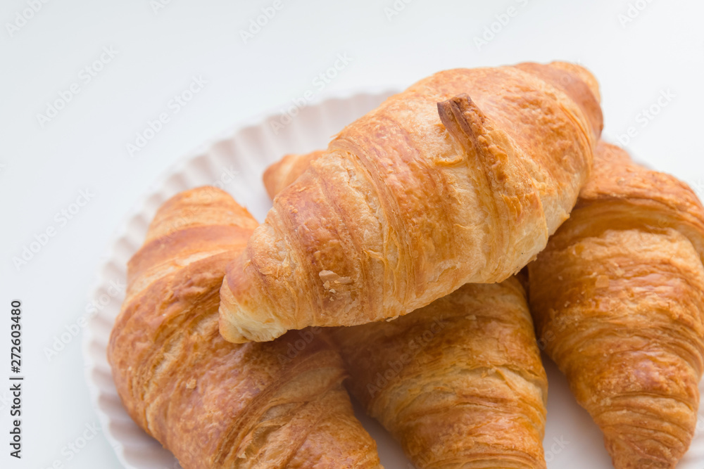 Plain croissants on top of each other on the plate, white table