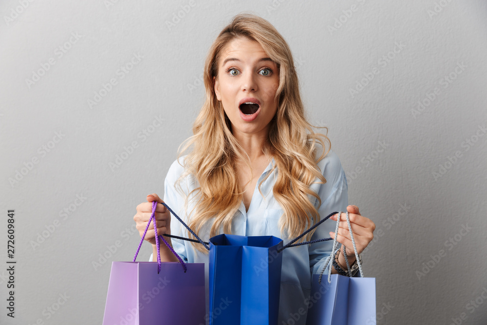 Shocked excited young pretty blonde business woman posing isolated grey wall background holding shopping bags. Shocked excited young pretty blonde business woman posing isolated grey wall background holding shopping bags.