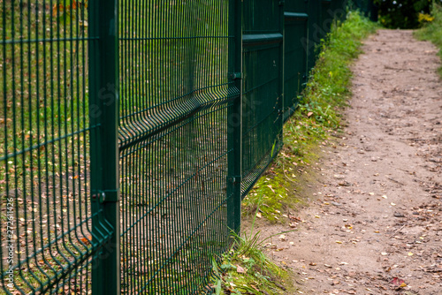 Empty path by the green metal fence