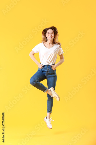 Jumping young woman in jeans on color background