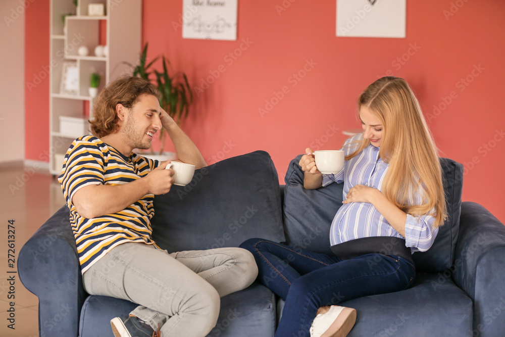 Happy young pregnant couple drinking tea at home