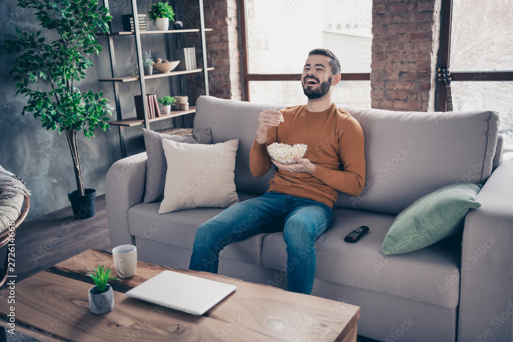 Portrait of his he nice-looking attractive bearded cheerful cheery positive guy spending weekend sitting on divan watching tv at industrial loft interior style living-room indoors