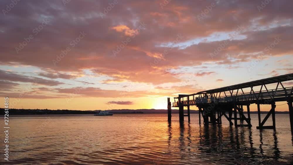 A passenger ferry passes by Northcote pier at sunset in Auckland city, New Zealand A passenger ferry passes by Northcote pier at sunset in Auckland city, New Zealand