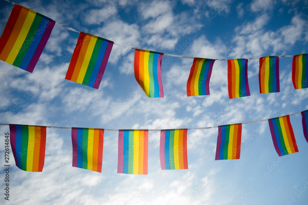 Two strands of celebratory gay pride rainbow flag bunting fluttering backlit by the sun against blue sky copy space