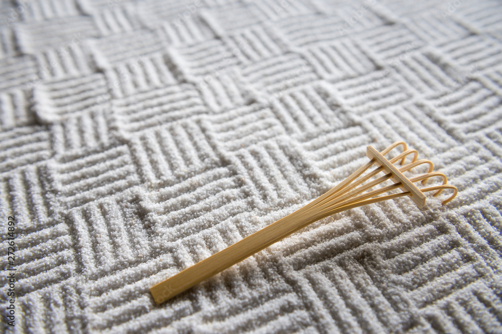 Bamboo rake resting on woven cross-hatch pattern raked into an abstract textured background in the monochrome white sand gravel of a Japanese Zen garden Bamboo rake resting on woven cross-hatch pattern raked into an abstract textured background in the monochrome white sand gravel of a Japanese Zen garden
