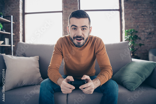 Portrait of his he nice-looking attractive bearded cheerful cheery addicted guy spending weekend sitting on divan playing xbox at industrial loft brick interior style living-room indoors