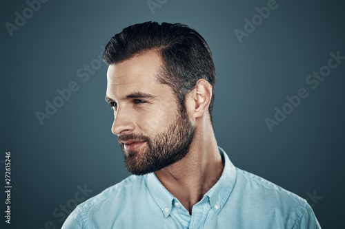 So charming! Handsome young man smiling and looking away while standing against grey background