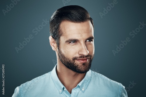 Male beauty. Handsome young man smiling and looking away while standing against grey background