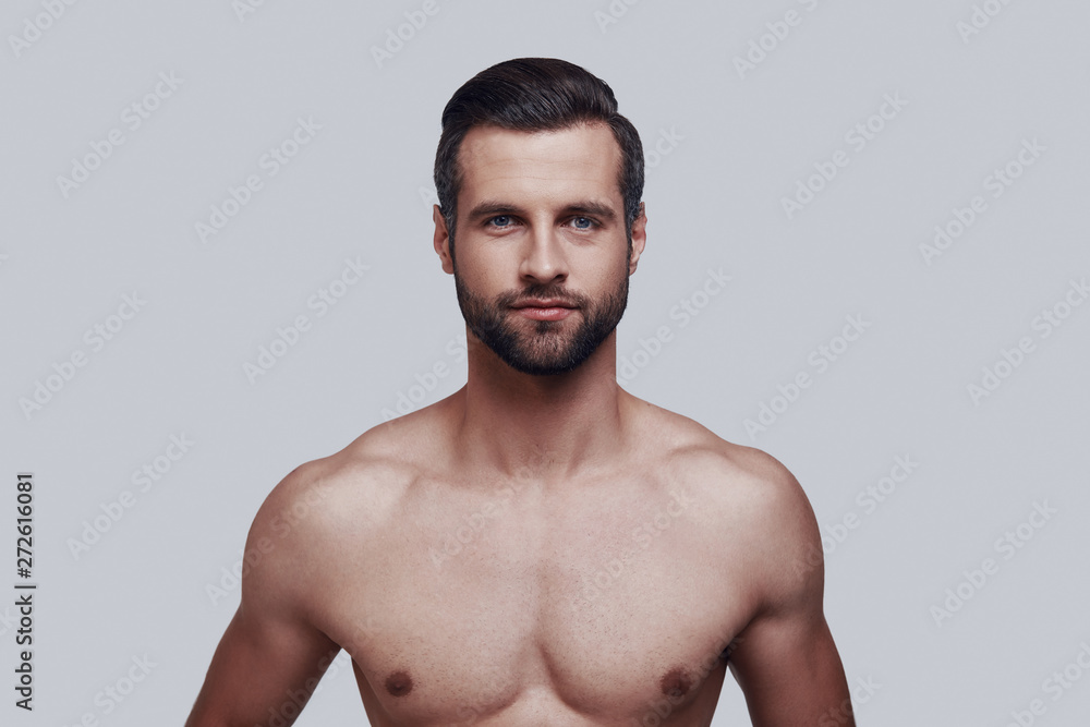 Fototapeta premium Young and handsome. Handsome young man looking at camera and smiling while standing against grey background