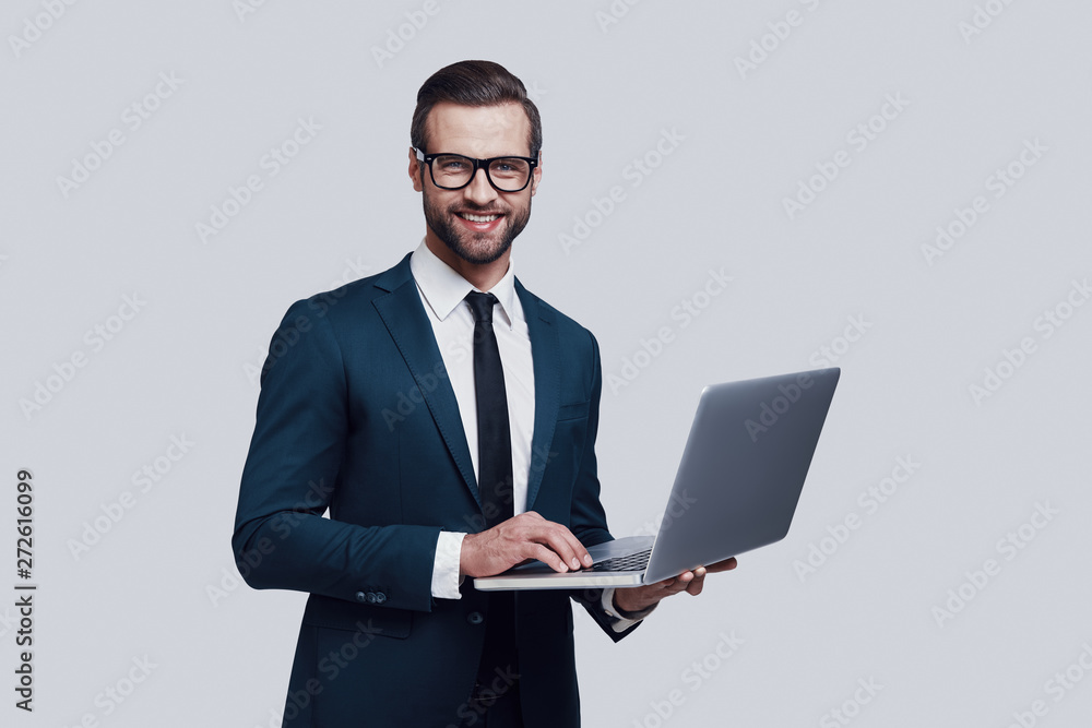 May I help you? Handsome young man looking at camera and smiling while standing against grey background May I help you? Handsome young man looking at camera and smiling while standing against grey background