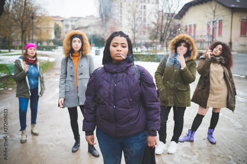 group of young multiracial women smoking cigarette in the street
