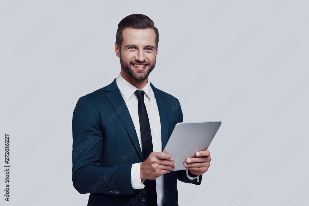 Always ready to help. Handsome young man working using digital tablet while standing against grey background Always ready to help. Handsome young man working using digital tablet while standing against grey background
