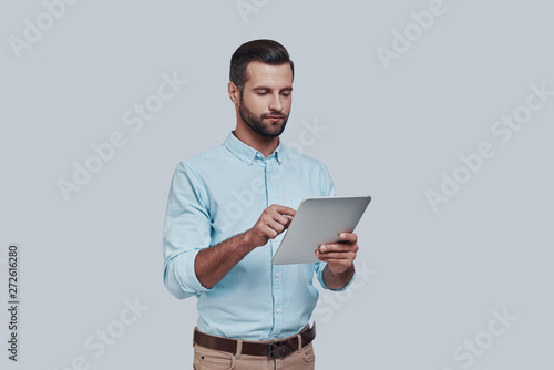 Planning new business. Handsome young man using digital tablet while standing against grey background