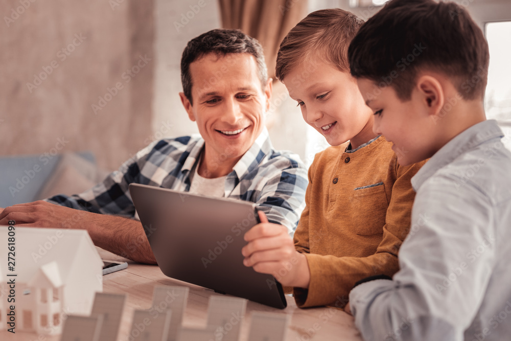 Fototapeta premium Two cute sons showing their photos to foster father on tablet