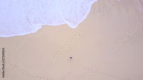 Aerial drone footage with ocean waves on white sand beach are moving to lonely girl. High top view. Relax bay and clean water.