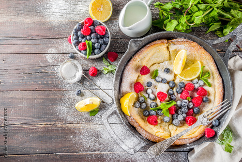 Sweet breakfast vegan dutch baby baked pancake with fruit and berries, wooden background copy space