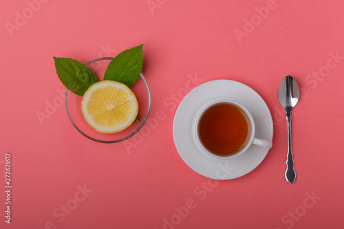 White cup of tea and fresh lemon on a pink background.