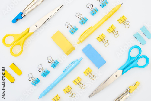 flat lay of yellow and blue erasers, pens, scissors, compasses and paper clips isolated on white