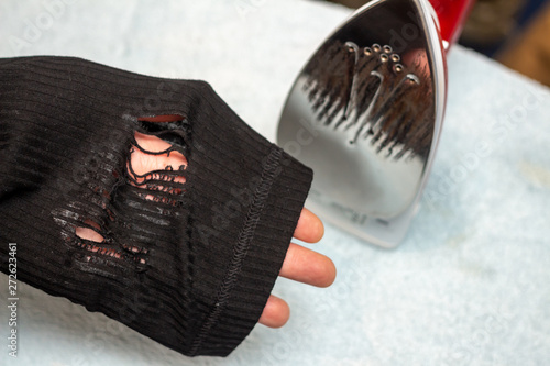 The molten fibers of the synthetic fabric of the garment after using a highly heated iron. Permanently damaged clothing. The molten hole in the fabric or severely scorched clothes. Household concept