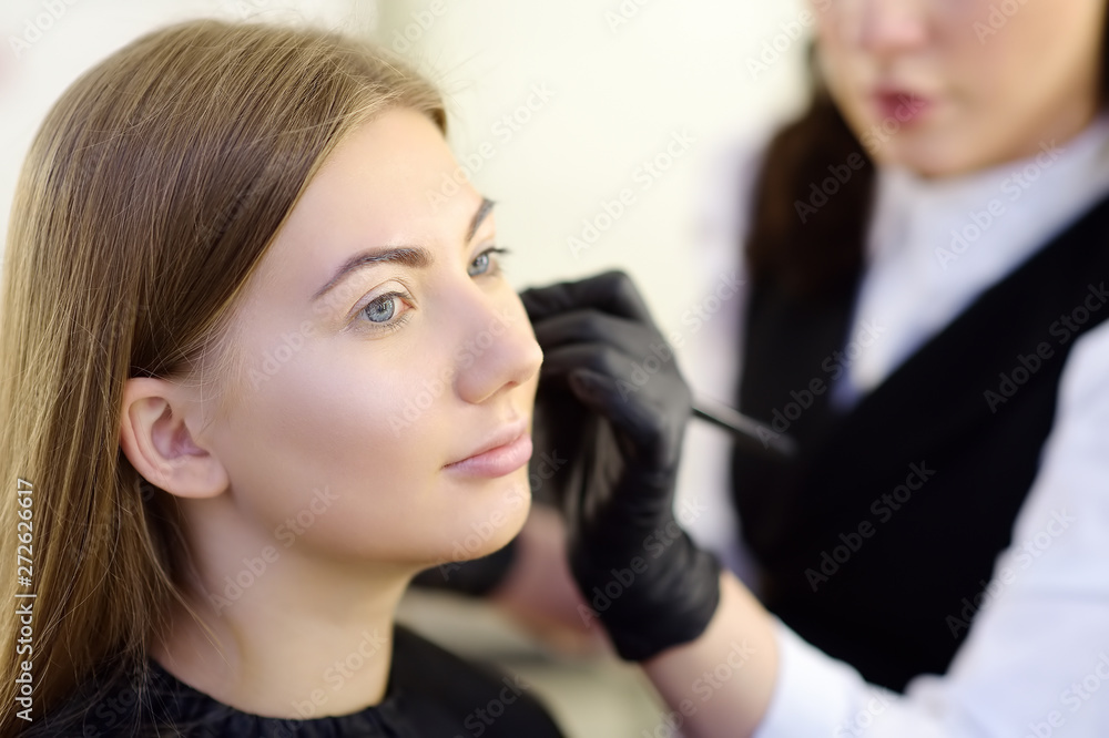 Beautician applying the tone of the foundation using special brush on face young beautiful model. Facial care and make up Beautician applying the tone of the foundation using special brush on face young beautiful model. Facial care and make up