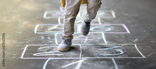 Closeup of little boy's legs and hopscotch drawn on asphalt. Child playing hopscotch game on playground outdoors on a sunny day.