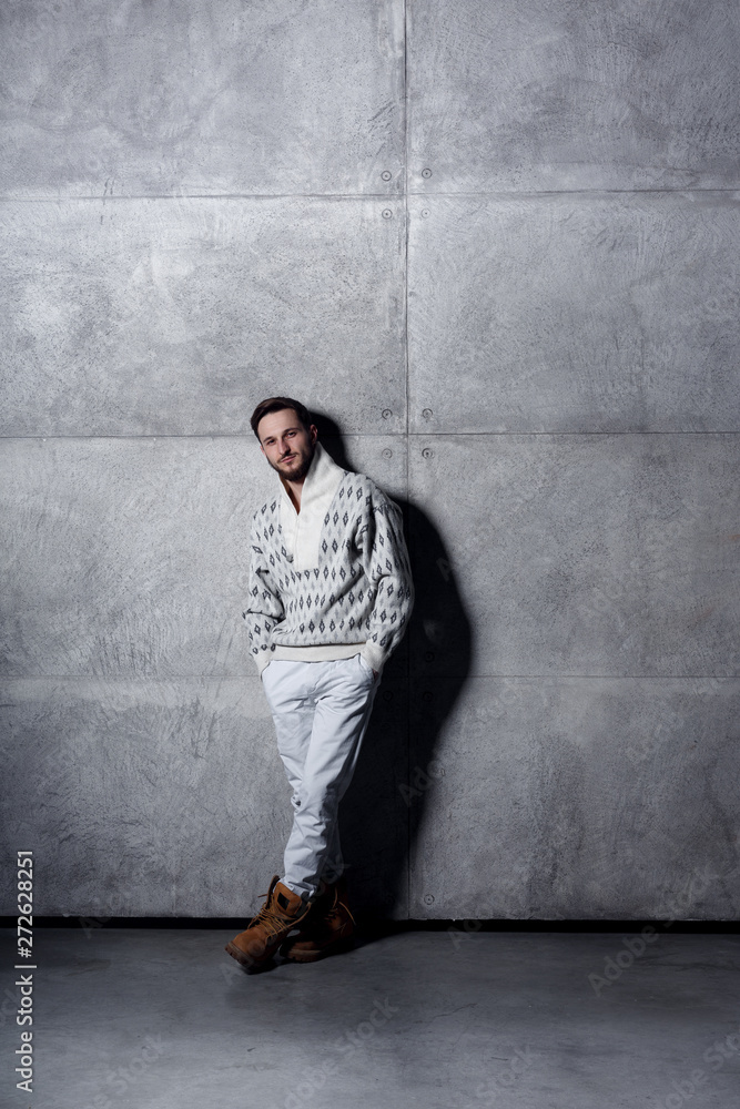 Full length isolated studio portrait of a young man in white jeans and cardigan, posing over concrete background. Full length isolated studio portrait of a young man in white jeans and cardigan, posing over concrete background.