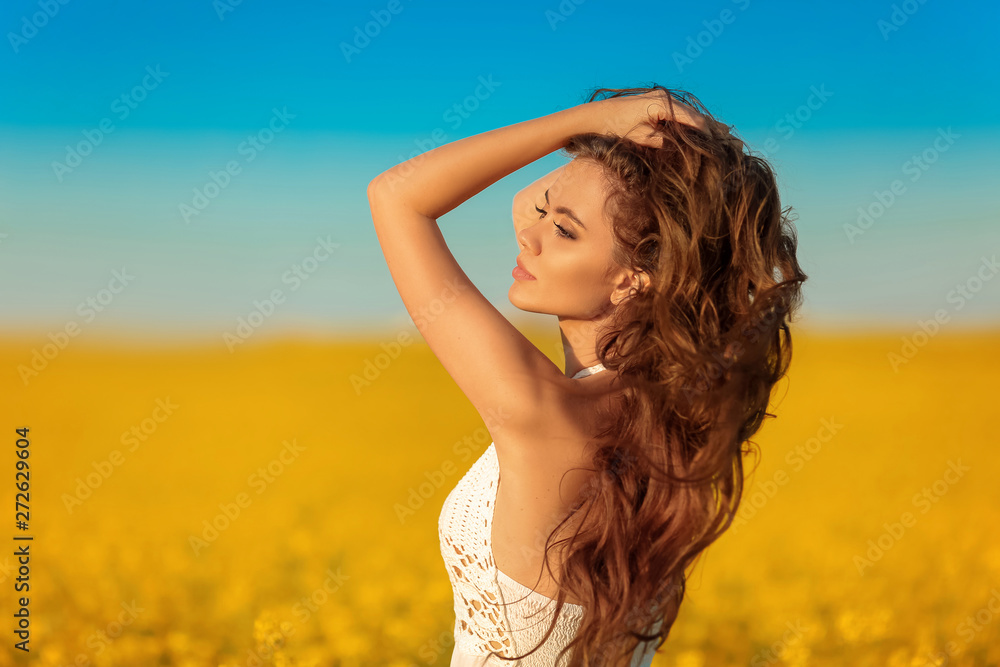 Beautiful carefree girl with long curly healthy hair over Yellow rape field landscape background. Attracive brunette with blowing hairstyle enjoying and breathing sunset, outdoor beauty portrait. Beautiful carefree girl with long curly healthy hair over Yellow rape field landscape background. Attracive brunette with blowing hairstyle enjoying and breathing sunset, outdoor beauty portrait.