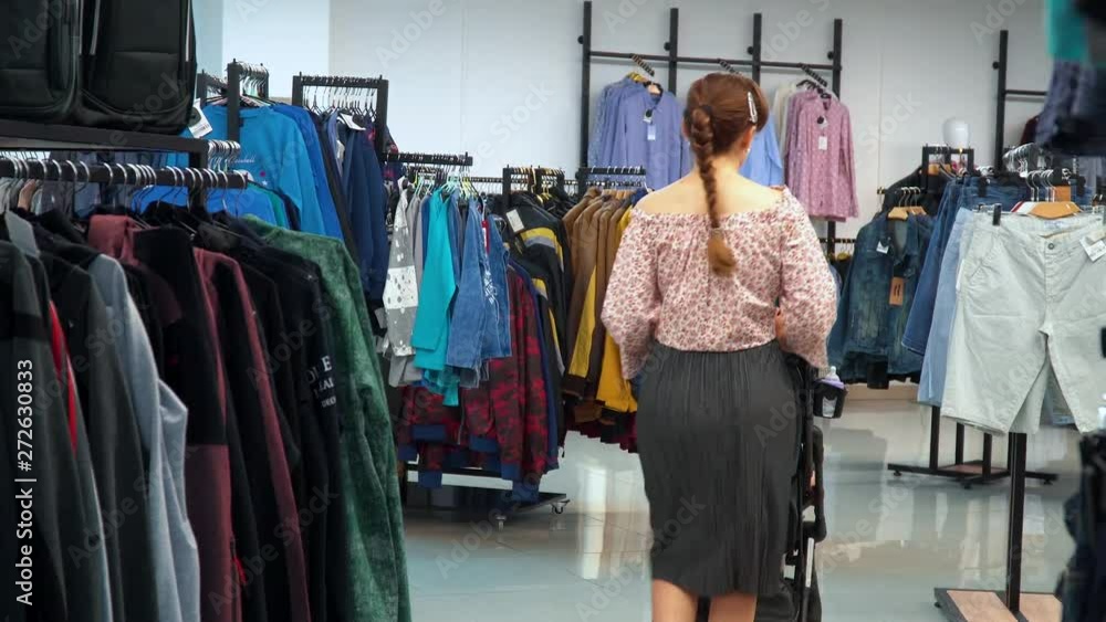 Young woman with a child goes to the store and chooses clothes Young woman with a child goes to the store and chooses clothes